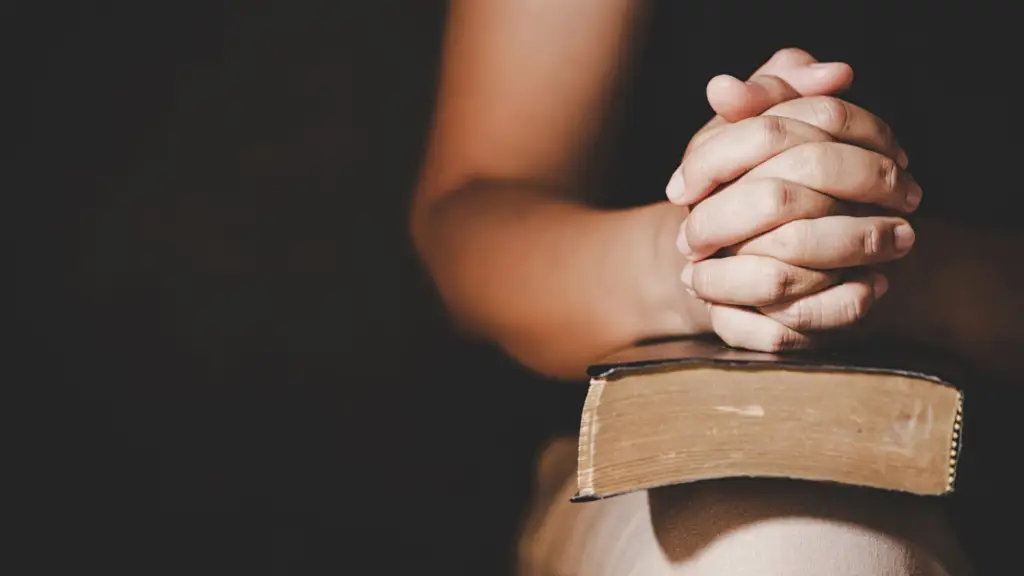 A young woman with hands clasped in prayer resting her hands on a bible