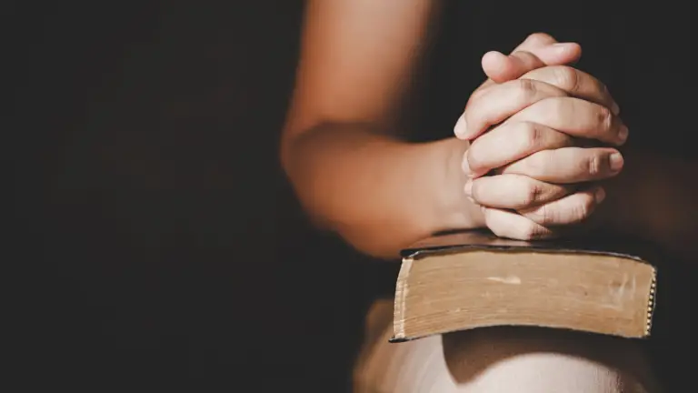 A young woman with hands clasped in prayer resting her hands on a bible
