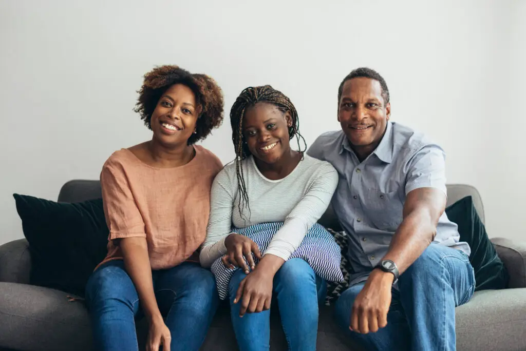Parents and daughter sitting on a gray couch.
