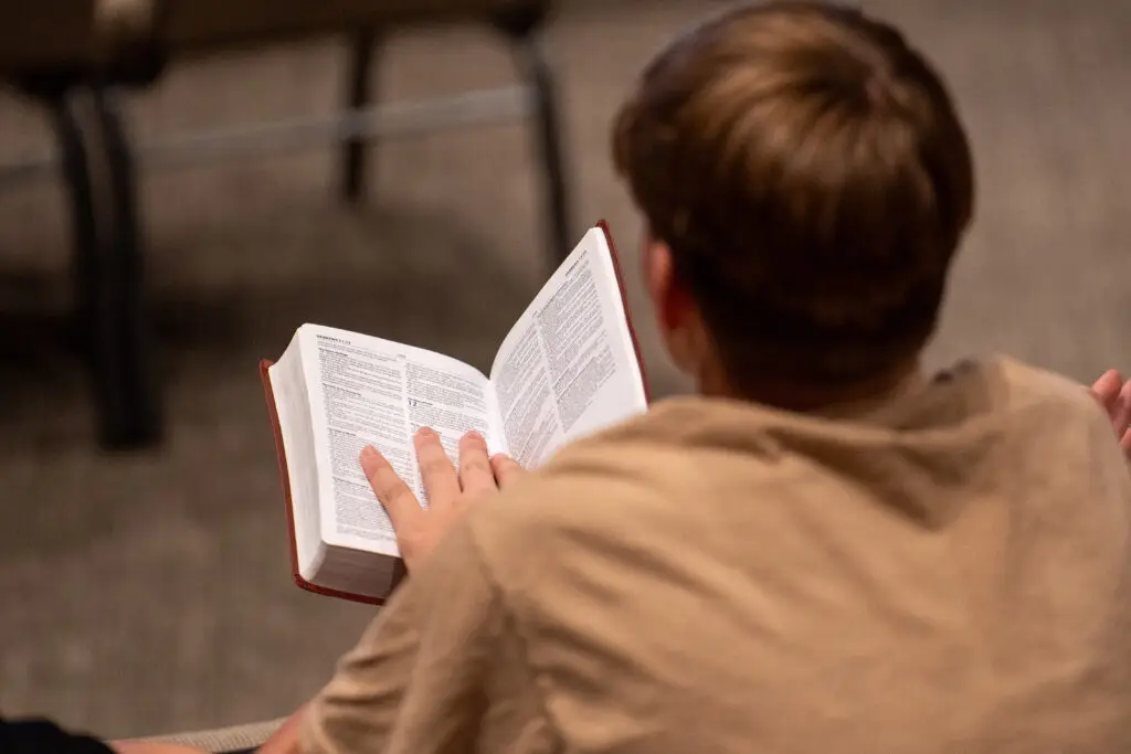 View from behind a teenager seated holding his Bible open to Hebrews 12.