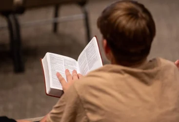 View from behind a teenager seated holding his Bible open to Hebrews 12.